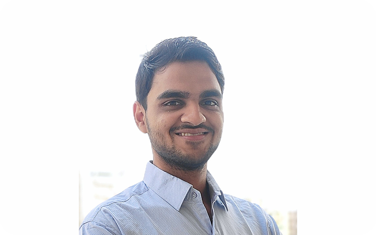 Smiling man in a light blue shirt with short hair, standing outdoors against a bright background.