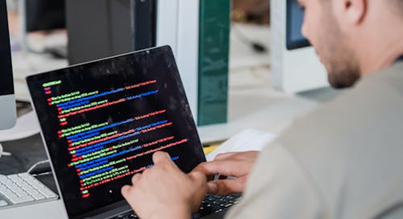 Man coding on laptop in office, focused on colorful code, software development, tech environment.