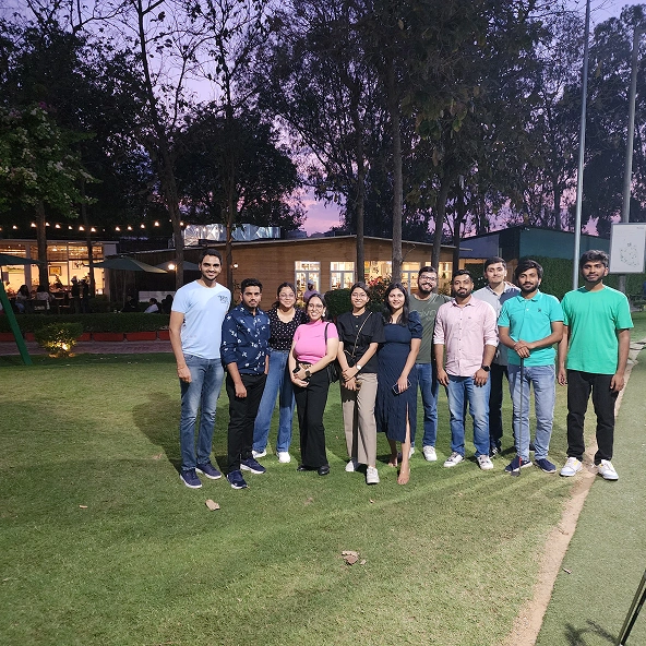 Group of friends posing on grass at scenic outdoor venue with sunset view.