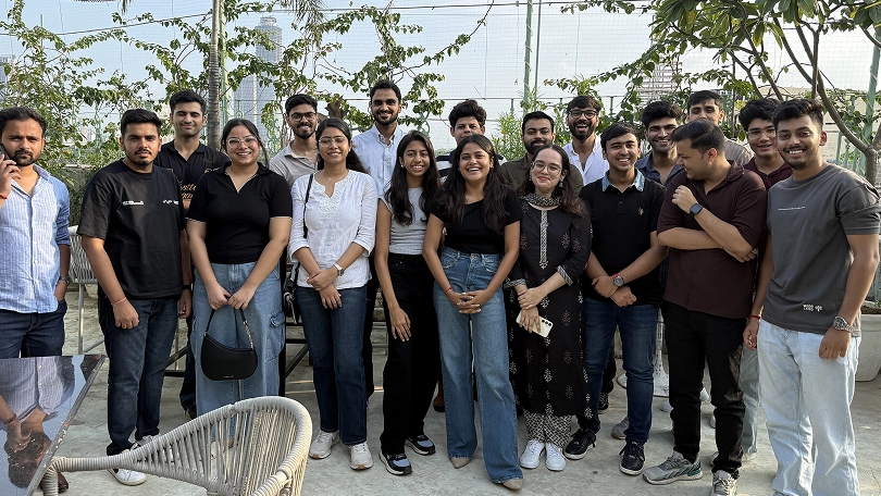 Group of people smiling outdoors, standing together on a sunny day with greenery in the background.
