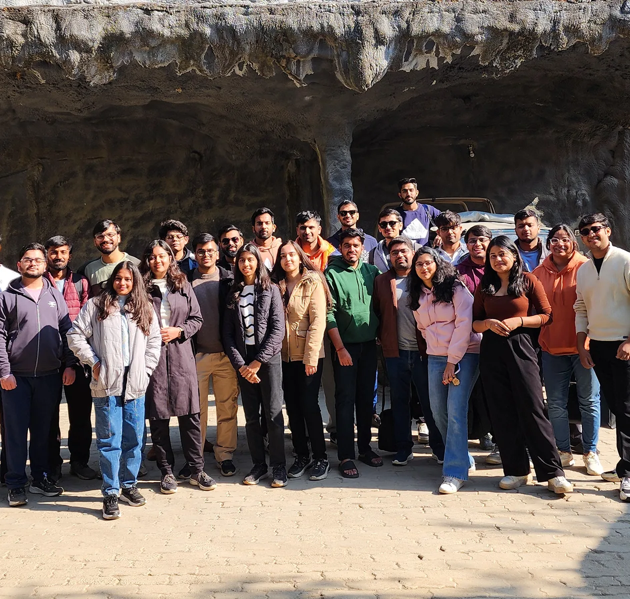 Group photo of smiling people standing outdoors in front of a rocky background, enjoying a sunny day.