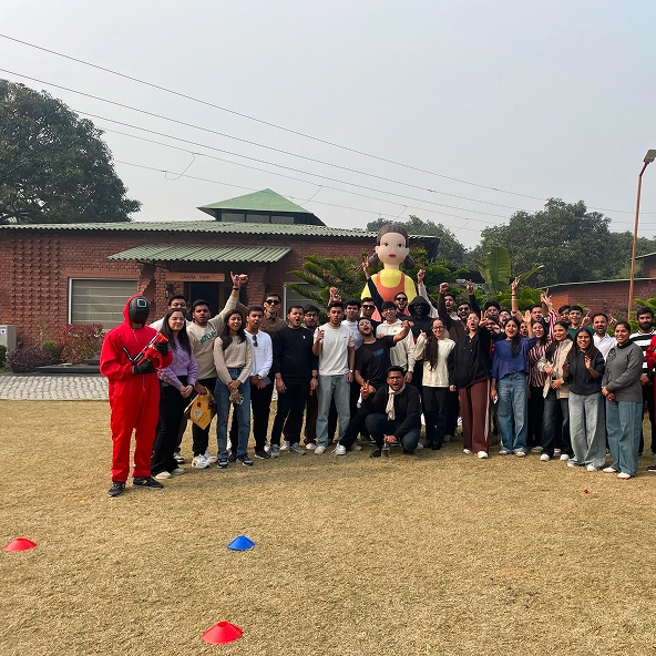 Group of people gathered outdoors for a team-building event, posing with a mascot and a person in a red costume.