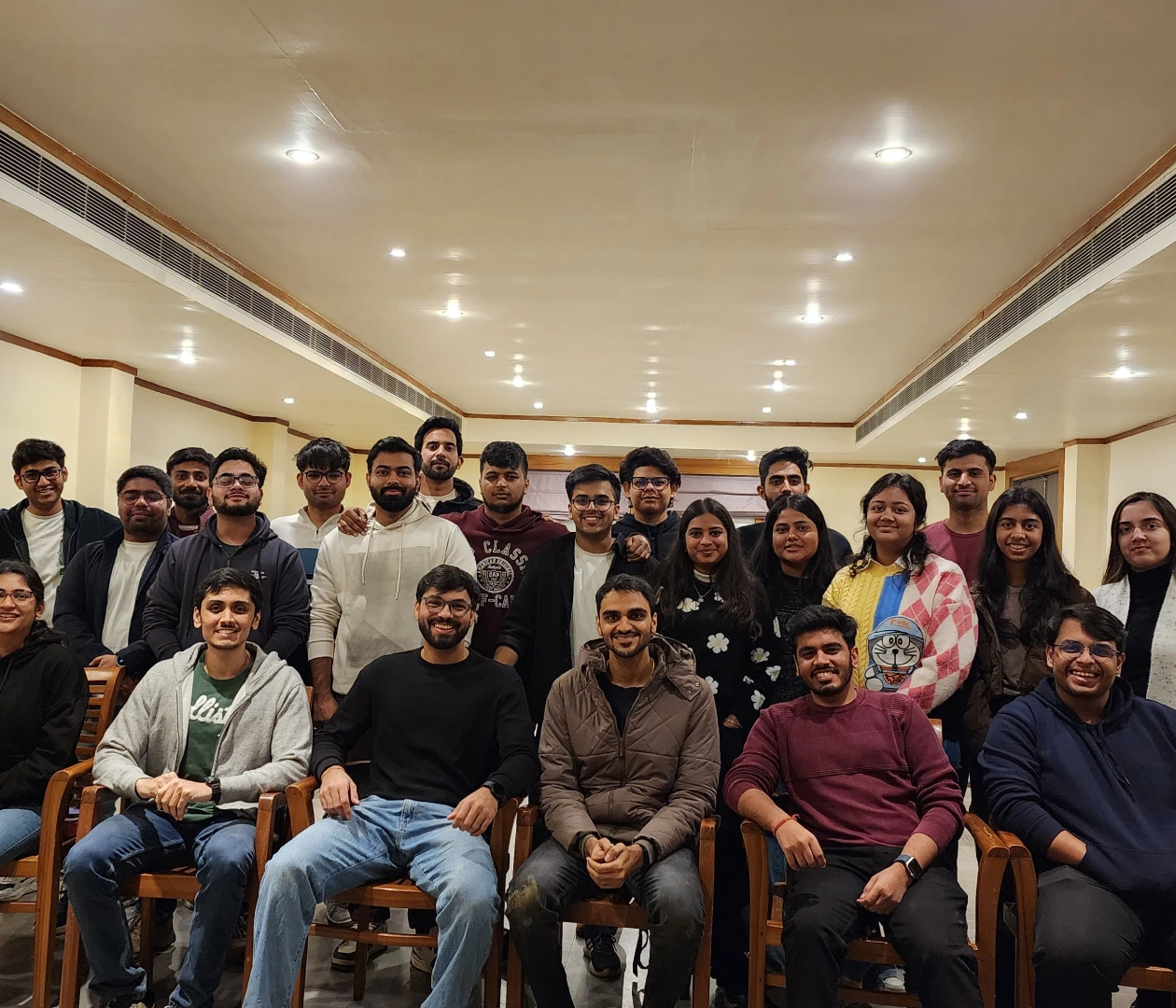 A group of smiling young adults gathers indoors for a team photo, showcasing camaraderie and teamwork.