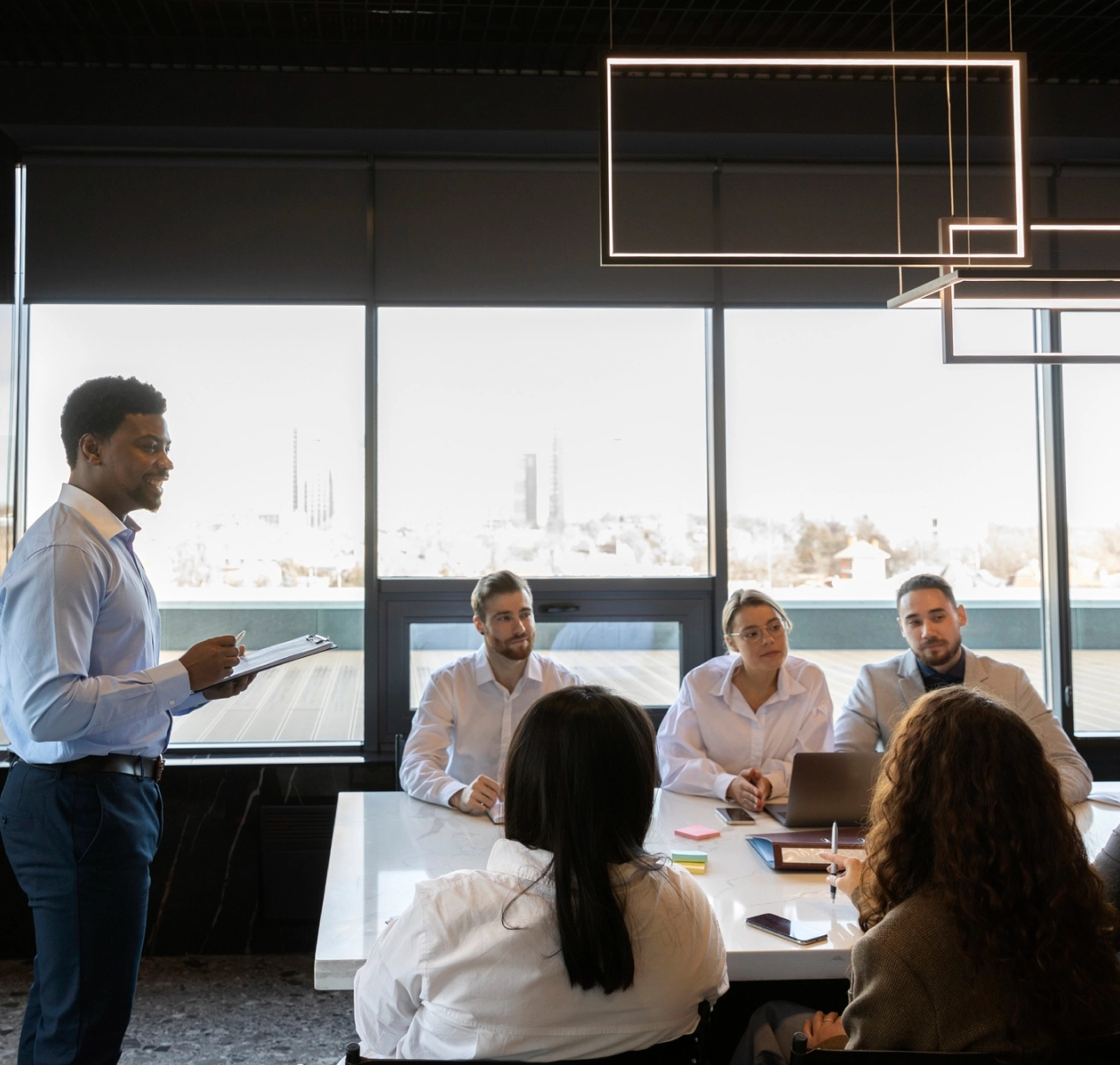 A diverse team in a modern office engaged in a productive meeting led by a presenter with a clipboard.