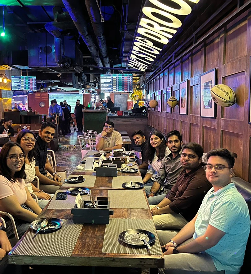 A group of friends enjoying a meal in a lively, modern restaurant setting, smiling and seated around a long table.