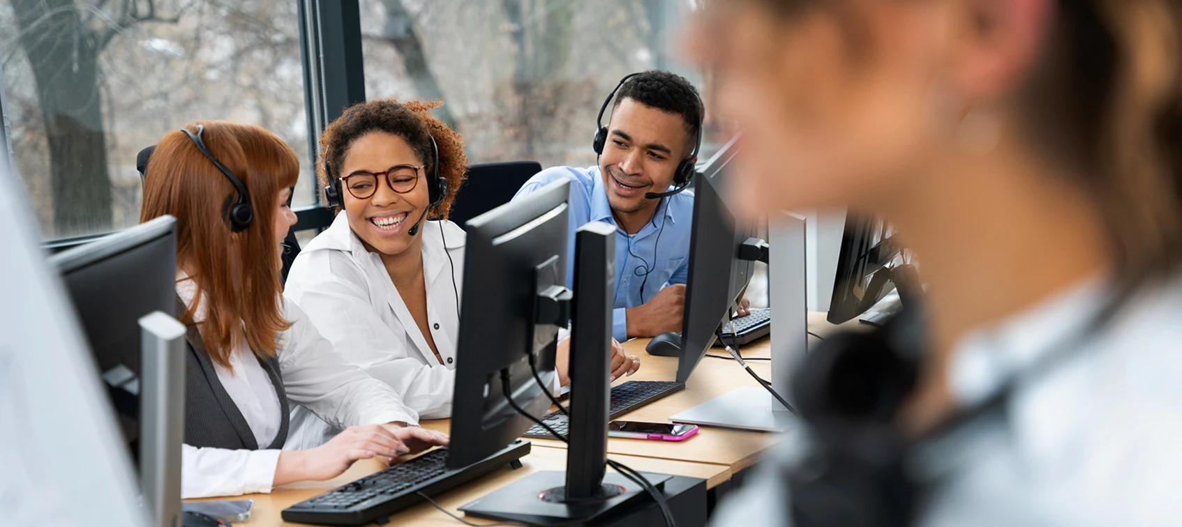 Team in an office wearing headsets, collaborating at computers, engaging in work discussions.