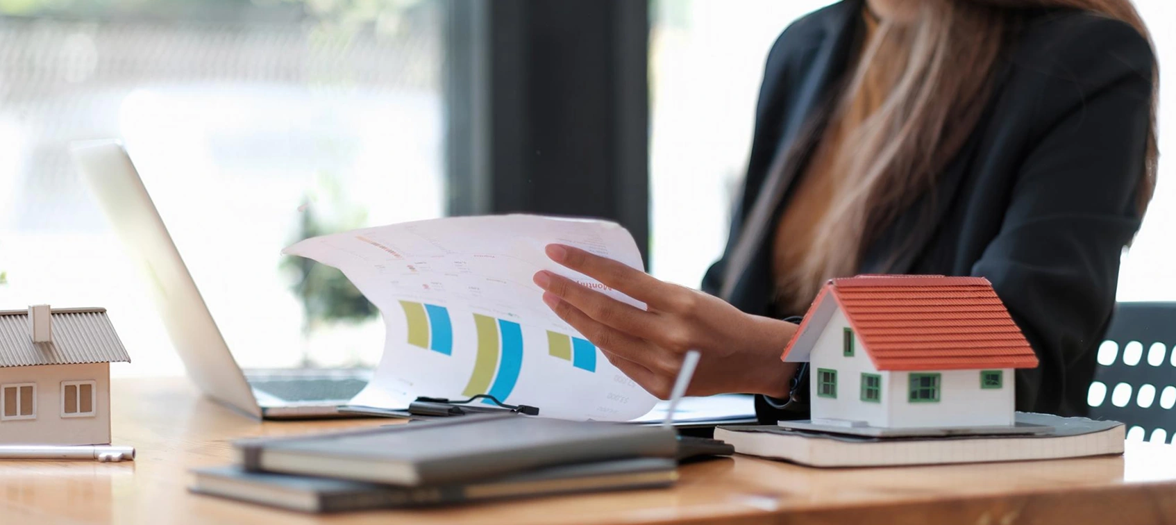 Real estate agent reviewing documents near house models on desk.