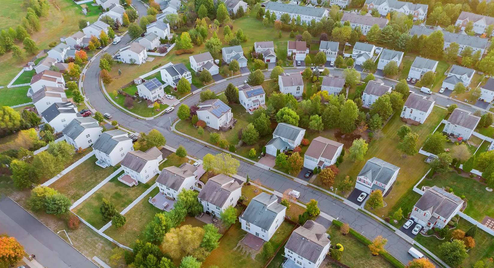 Aerial view of suburban neighborhood with houses and green trees lining curving streets in a tranquil setting.